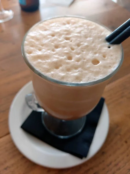 stock image Glass cup of ice coffee with whipped milk on a wooden table.