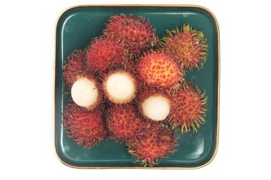 Yarısı kesilmiş ve taze organik rambutan lezzetli meyveler beyaz arka planda izole edilmiş yeşil bir plaka manzaralı.