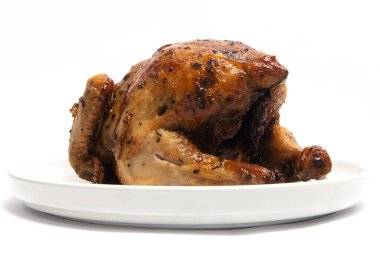 Beyaz arka planda izole edilmiş beyaz bir tabakta otlarla tatlandırılmış leziz bir kızarmış tavuk.