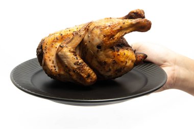 Beyaz arka planda izole edilmiş siyah bir tabakta otlarla tatlandırılmış lezzetli bir kızarmış tavuk.