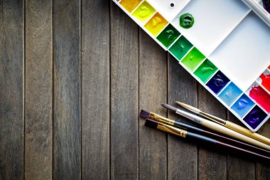 Boya fırçalarının üst görüntüsü palet ve beyaz kağıtlı suluboya boyalar. Kopyalama alanı olan resim ve metin iletisi ekle.