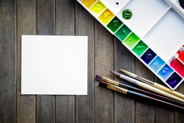 Boya fırçalarının üst görüntüsü palet ve beyaz kağıtlı suluboya boyalar. Kopyalama alanı olan resim ve metin iletisi ekle.