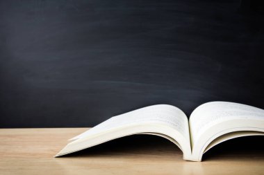 Back to school concept. Open book on table with blackboard backdrop copy space for art work design or add text message.