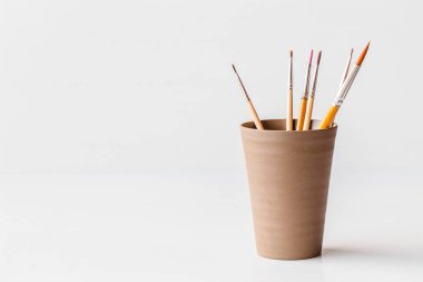 Beyaz arkaplanda izole edilmiş seramik bardaktaki fırçaları boyar