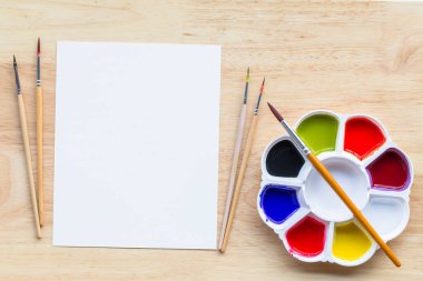 Top view of paintbrushes palette and watercolor paints with white paper on painted wooden planks. picture with copy space and for add text.