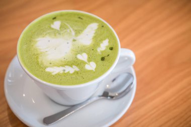 Bir fincan sıcak kibritli latte yeşil çay ve ahşap masada kaşık. Görüntünün alan derinliği sığ.