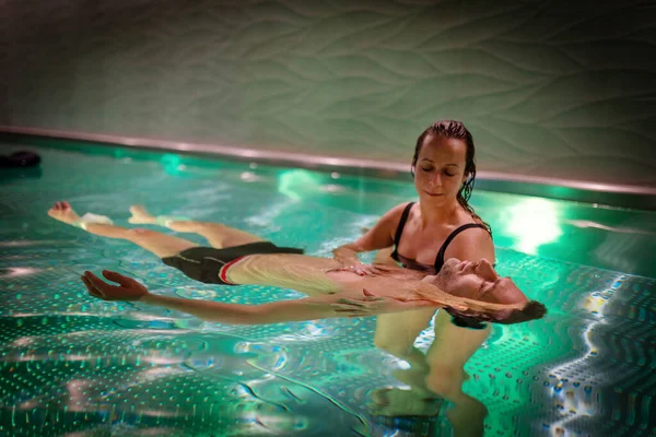 Therapeutic exercise in the pool. Woman receiving an aquatic therapy in the pool. Water relaxation and deep meditation