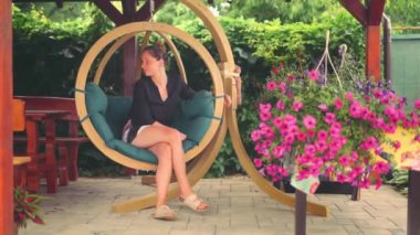 beautiful woman sits on a wooden swing surrounded by flowers