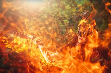 Şamanik tüy maskeli ve ormanlık alanda tarihi elbisesi olan bir kız. Ateş etkisi