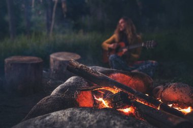 Büyüleyici bir sahne başlıyor. Bir kadın ustaca gitar çalıyor. Titreyen kamp ateşi sıcak bir parıltı bırakıyor. Bu gece bir ormanda toplanıp, samimi bir ortam yaratıyor..