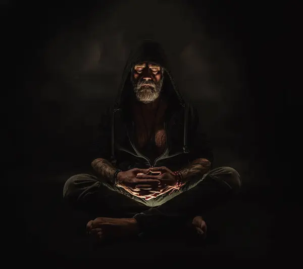 meditating man in a hood sits on the ground, man on the hands of the tattoo, atelier photos, black background