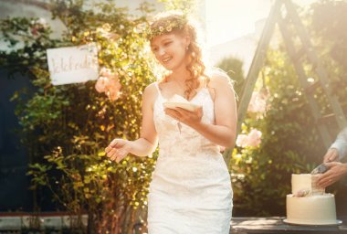 Gelin düğün pastası taşıyor. Neşeli gelin, çok özel gününün tadını çıkarıyor. Etrafı çarpıcı ve güzel bir bahçe düzeniyle çevrili.