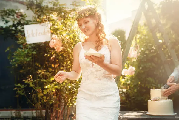 Gelin düğün pastası taşıyor. Neşeli gelin, çok özel gününün tadını çıkarıyor. Etrafı çarpıcı ve güzel bir bahçe düzeniyle çevrili.