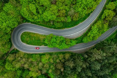 Kırmızı araba dağ boyunca serpentin asfalt yolu boyunca gidiyor. Güzel yeşil ormanın içinden geçen yol. Havadan görüldü. Gökyüzü manzaralı. Drone fotoğrafçılığı. 