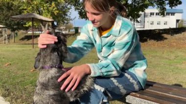 Gülümseyen sarışın kız yavru köpeğini kucaklıyor ve sonbahar parkında sarı yapraklarla hayvanlara sevgi ve özenle bakıyor. Güzel genç kız evcil köpeğiyle gezintiye çıkıyor.