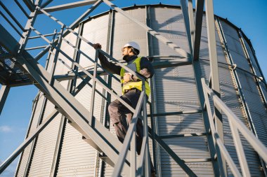 A supervisor climbs up on the silo with a tablet in his hands and checks on supplies. clipart