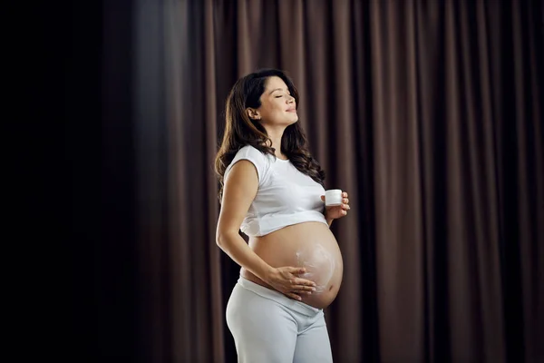 幸せな妊娠中の女性は 彼女の腹に反ストレッチマークローションを置いています — ストック写真