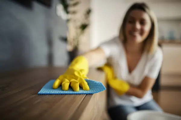A hand with rubber gloves cleaning furniture with cloth.