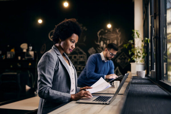 An african businesswoman is working with documents and scrolling on a laptop while working from office. — Stock Image African Businesswoman Working Documents Scrolling Laptop While Working Office Stock Picture