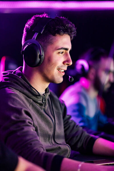 Smiling professional gamer with headset sits in gaming room and playing video games online. — Stock Image Smiling Professional Gamer Headset Sits Gaming Room Playing Video Games Royalty Free Stock Photos