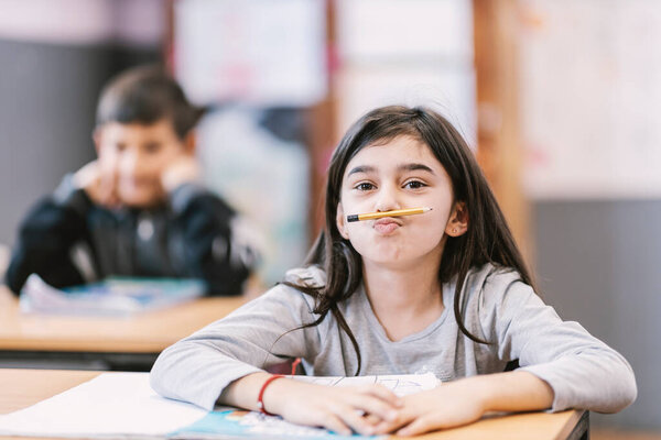 An Indian schoolgirl pretending pencil is mustache while sitting on class. — Stock Image Indian Schoolgirl Pretending Pencil Mustache While Sitting Class Stock Picture