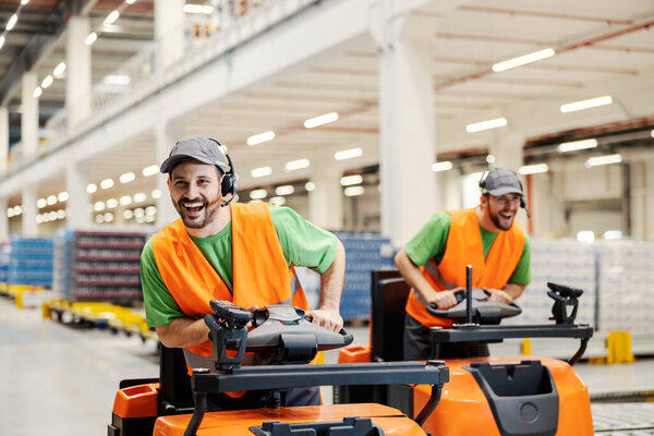 Two playful storage workers racing with forklifts in storage. — Stock Image Two Playful Storage Workers Racing Forklifts Storage Royalty Free Stock Images