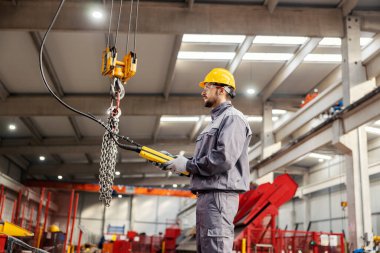 A metallurgy worker relocates heavy iron chains with the use of a hook. clipart