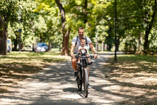 Family with healthy habits riding a bicycle in park on sunny day.