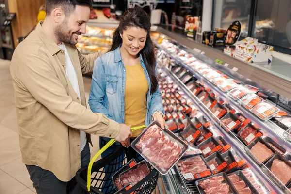 情侣们正在购物车里放生肉 并在超级市场上购买食品 — 图库照片