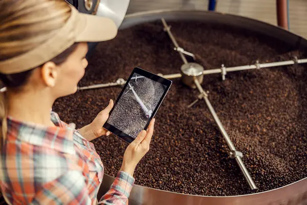 A coffee industry worker taking photo of coffee roasting machine working.