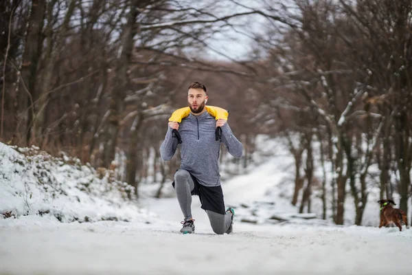 Sportsman doing lunges and holding weights in nature at snowy winter day. Bodybuilding, healthy habits, winter fitness