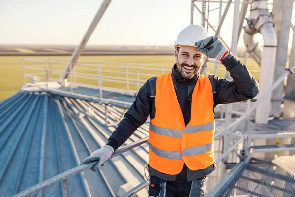 Portrait of industry worker standing on top of the silo and greeting visitors.