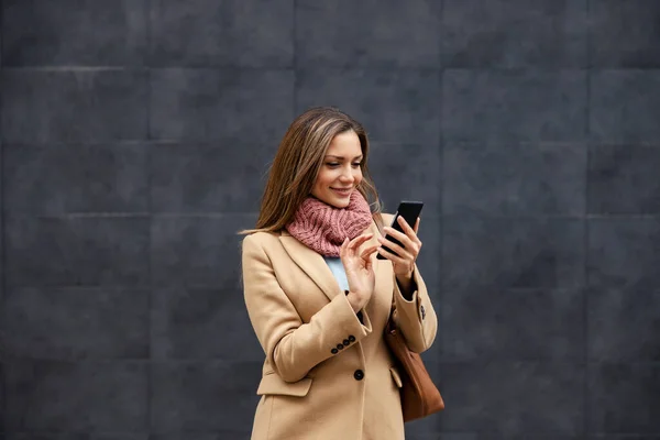 Telecommunications and 5g technology. A happy woman in a warm outfit standing outdoors and typing a message on her phone. A woman using her phone.