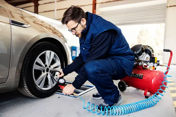 A car mechanic\'s worker checking on tire pressure on a car in garage.