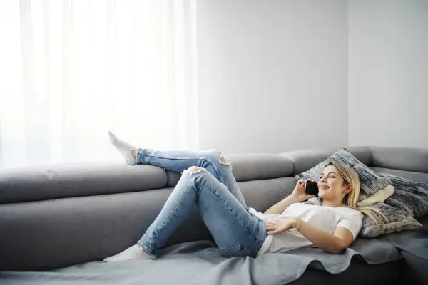 A woman relaxes on the sofa and having phone conversation at home.