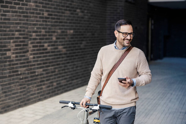 A smiling smart casual man pushes a bike on the street and uses his phone. — Stock Image Smiling Smart Casual Man Pushes Bike Street Uses His Phone Stock Picture