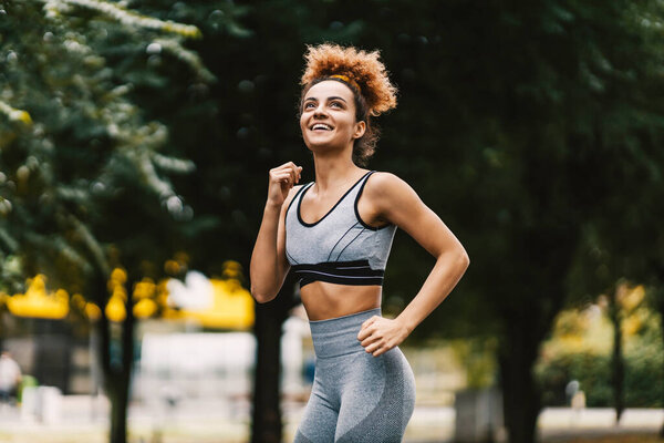 A happy slim urban runner is running in the city park with a toothy smile on her face. Fitness everywhere anytime. Urban runner running in the park. — Stock Image Happy Slim Urban Runner Running City Park Toothy Smile Her Stock Image