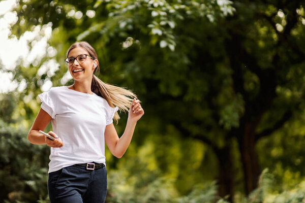 A happy girl walking in the public park, spending the day in nature, and listening to her favorite radio station on the phone. A girl with a phone listening to music in nature — Stock Image Happy Girl Walking Public Park Spending Day Nature Listening Her Stock Image