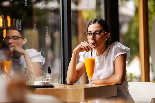A college girl is sitting in a bar, sipping fresh orange juice on a break between lectures. A healthy way to kill time. A girl in a bar drinking juice — Stock Image College Girl Sitting Bar Sipping Fresh Orange Juice Break Lectures Royalty Free Stock Photos