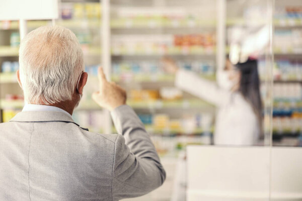 Rear view of a senior man pointing at the shelf with medicines. — Stock Image Rear View Senior Man Pointing Shelf Medicines Stock Image
