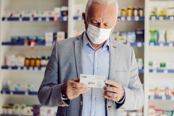 A senior citizen with mask holding box with pills and reading instructions. — Stock Image Senior Citizen Mask Holding Box Pills Reading Instructions Royalty Free Stock Photos