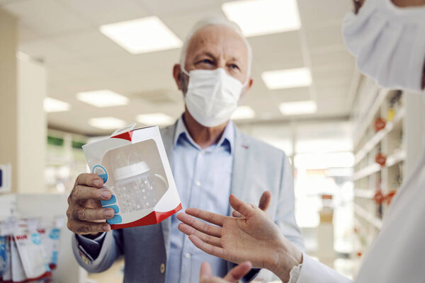 An old man asking for opinion apothecary worker about baby bottles. — Stock Image Old Man Asking Opinion Apothecary Worker Baby Bottles Stock Image