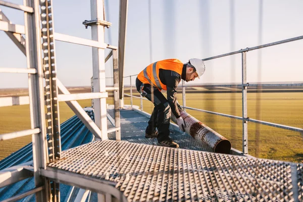 An industry worker is relocating metal pipe while standing on top of the metal construction.