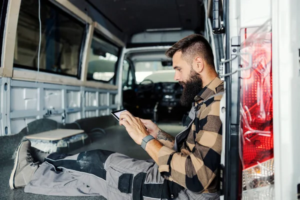 An auto mechanic sitting in a pickup truck and using tablet for problem diagnostics.