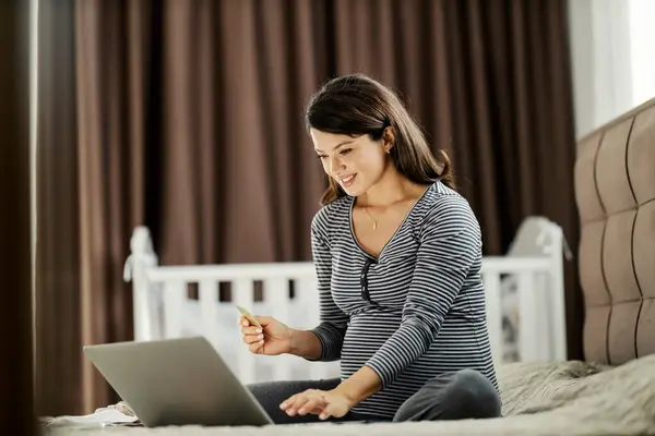 Šťastná Těhotná Žena Sedí Posteli Nakupuje Online Dětské Věci Zatímco — Stock fotografie