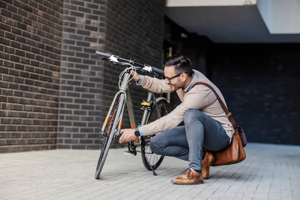 カジュアルなビジネスマンが路上で曲がりながら自転車を修理しています — ストック写真