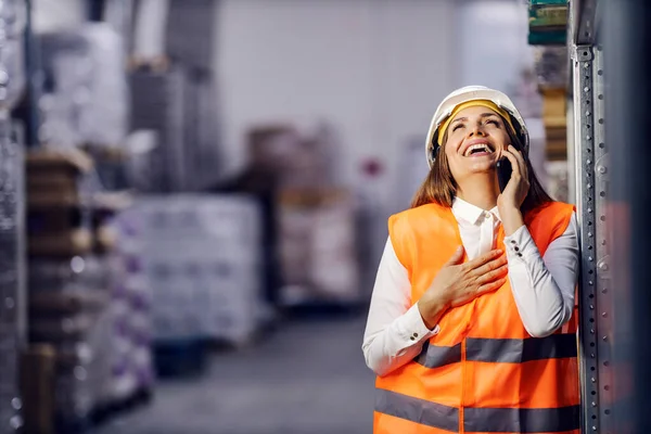 A businesswoman is laughing while standing in facility and have phone call.