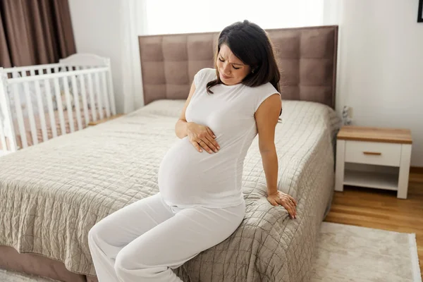 妊娠中の女性が寝室に座って赤ちゃんが蹴っていると感じています — ストック写真