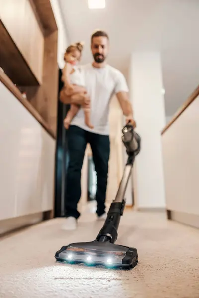 stock image Selective focus on a vacuum cleaner. A father is vacuuming floor while babysitting his baby.