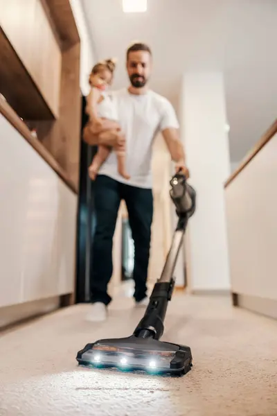 Stock image Selective focus on a vacuum cleaner. A father is vacuuming floor while babysitting his baby.